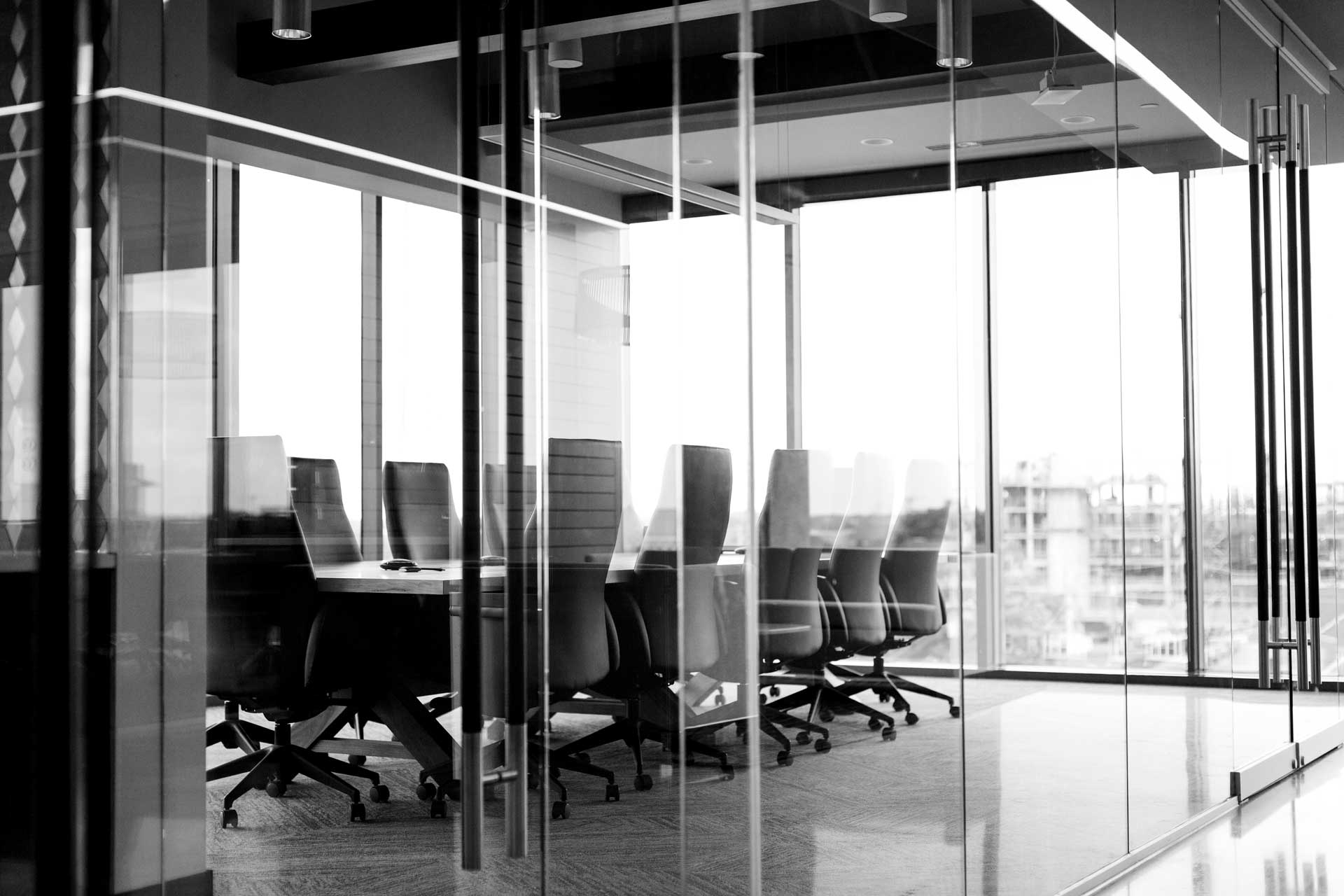 Black-and-white photo of conference table and several chairs behind glass doors and glass walls of empty conference room